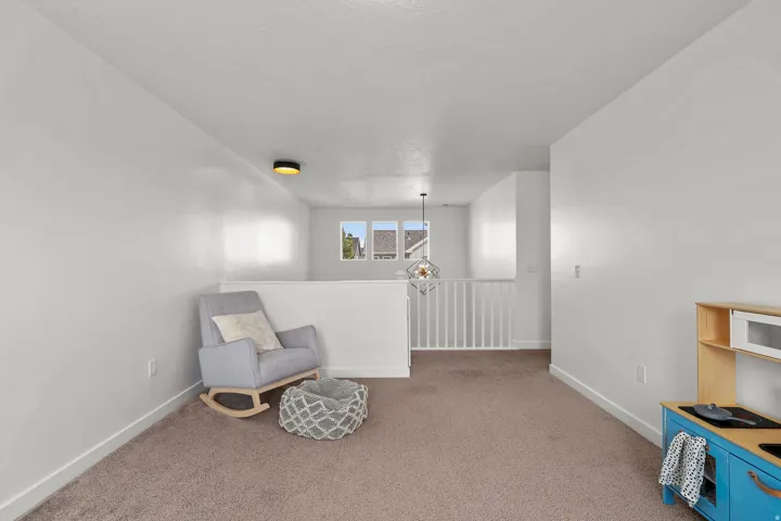 Carpeted room featuring white walls, a white railing, and a geometric pendant light fixture