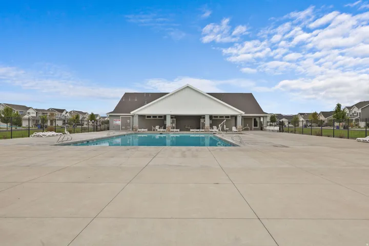 Community pool with a concrete deck and a clubhouse featuring a covered patio