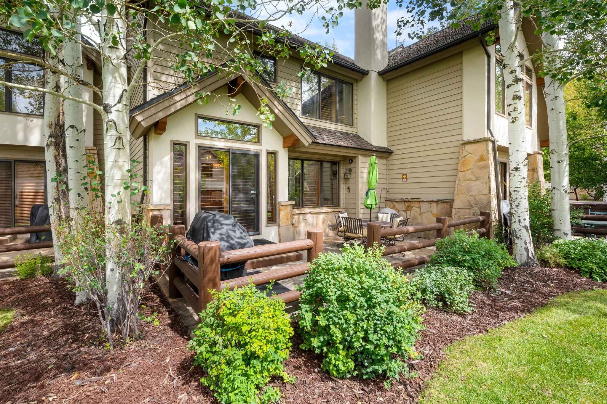 Stone and siding exterior with multiple patios, a stone chimney, a gabled window, and mature trees