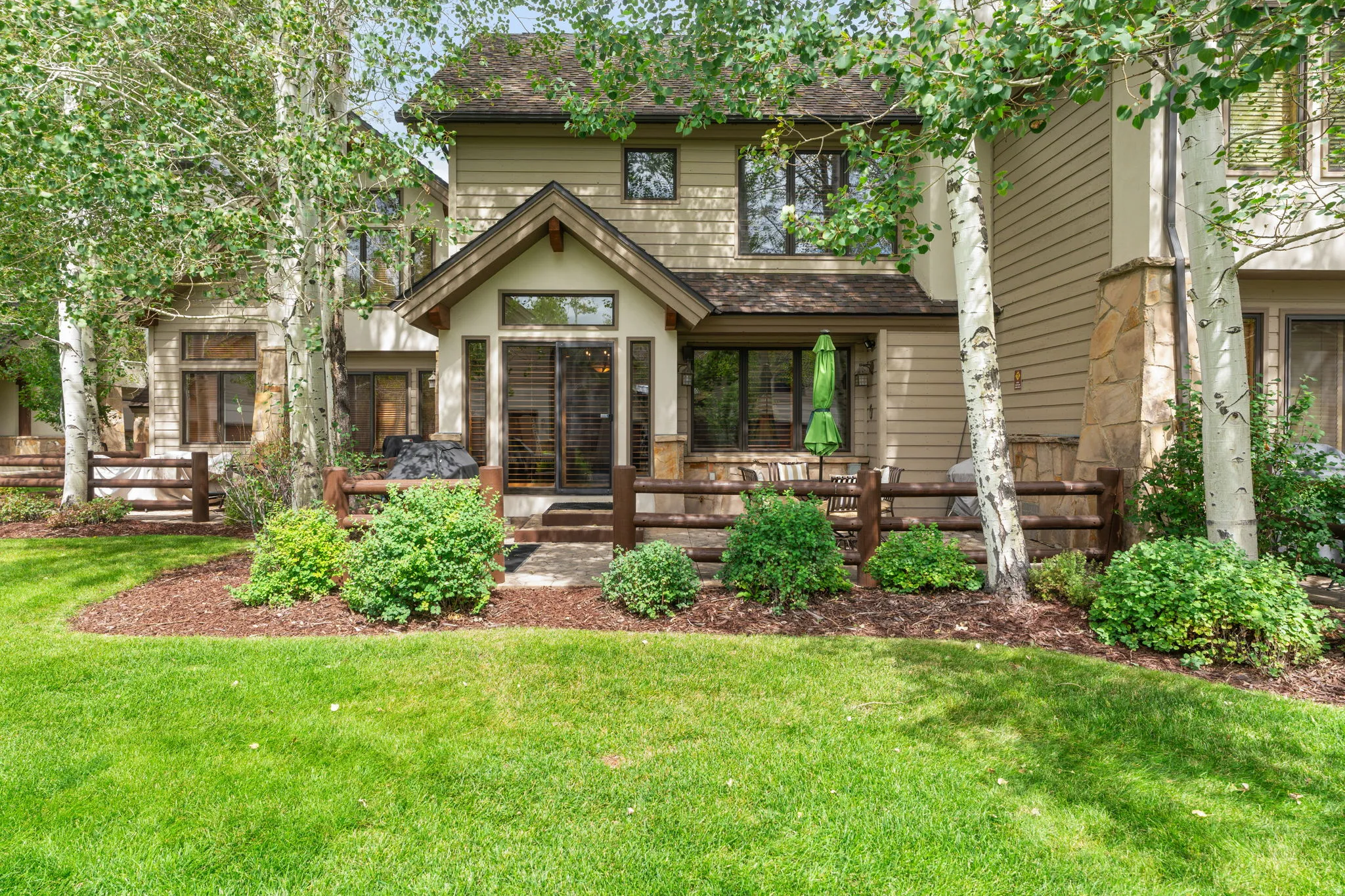 Exterior featuring a covered patio, sliding glass doors, stone column accents, wood-paneled siding, and mature trees