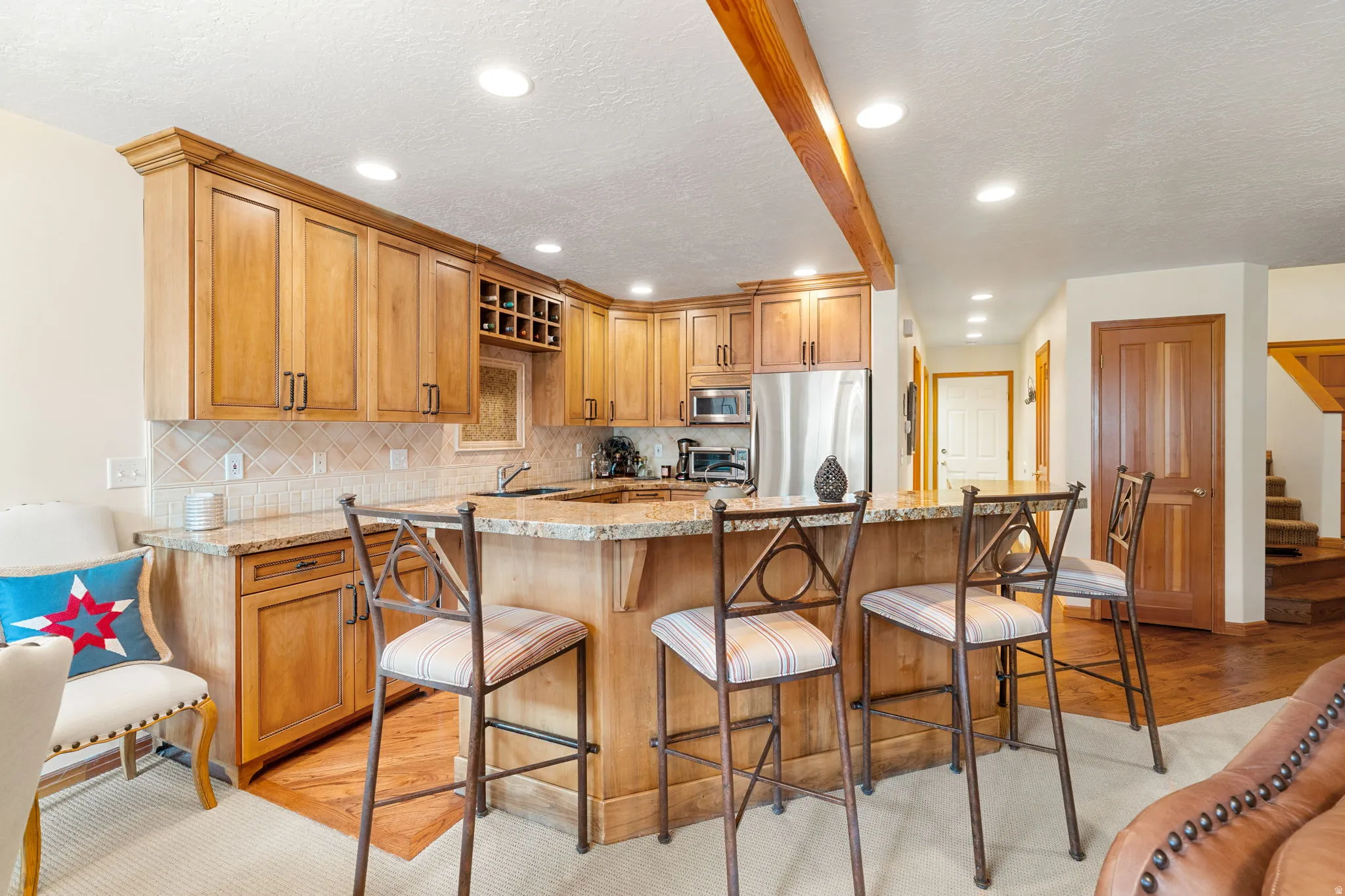 Kitchen featuring wood cabinetry, granite countertops, tile backsplash, built-in wine rack, and stainless steel appliances