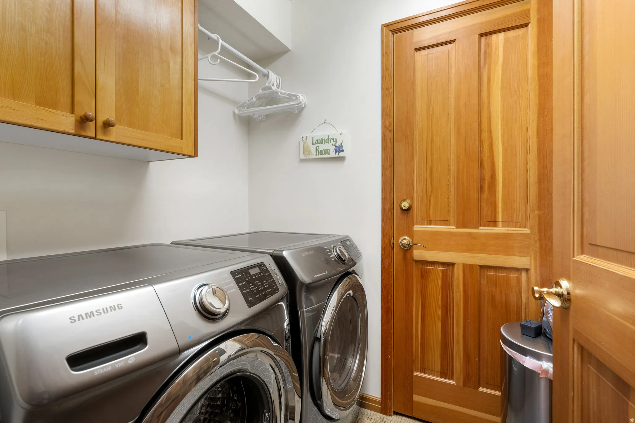 Recessed lighting with light wood-finish cabinetry, a built-in hanging rod, and a paneled wood-finish door with brass hardware