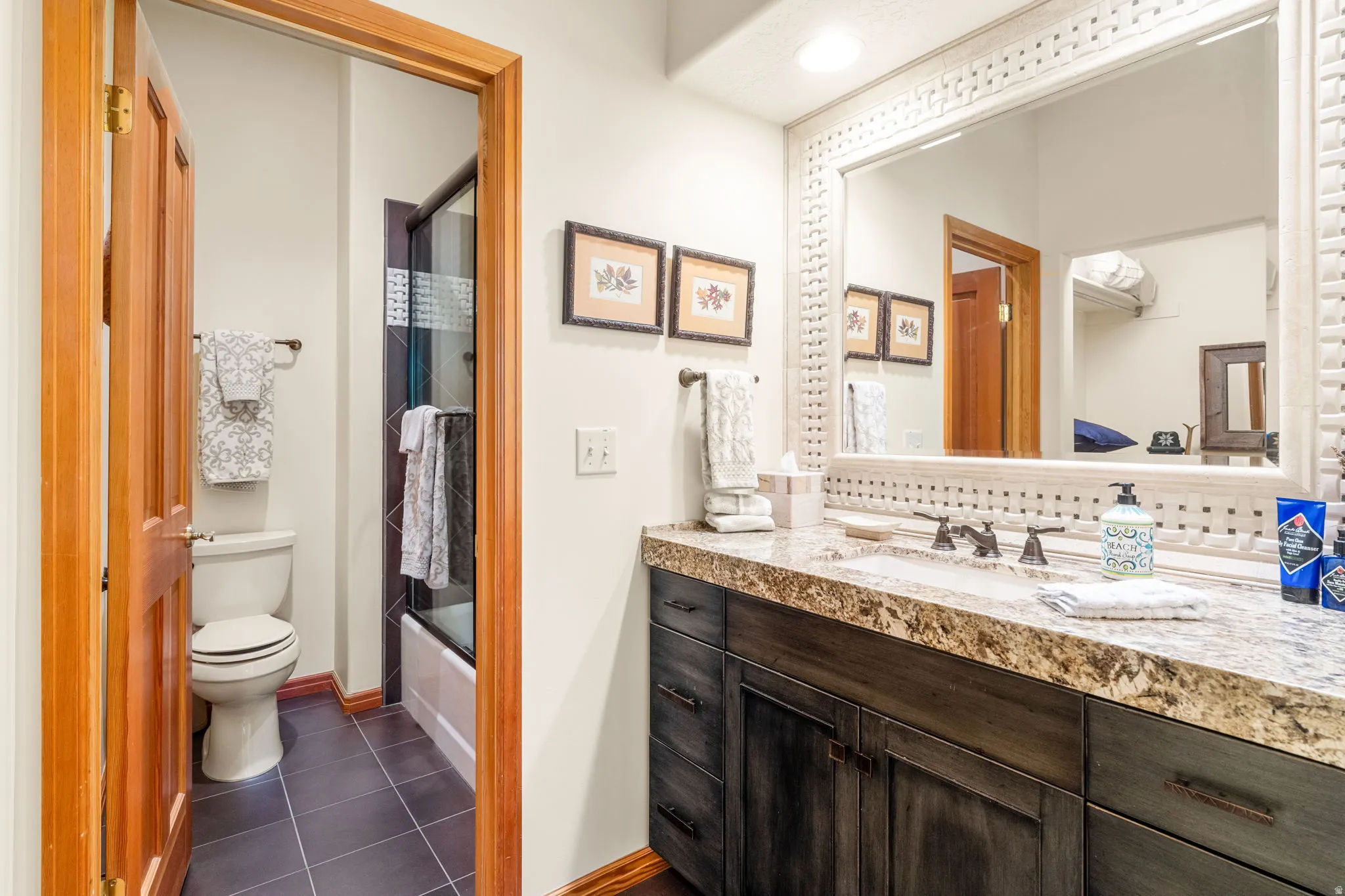 Vanity with a stone countertop, dark wood-finish cabinetry, and an ornate framed mirror