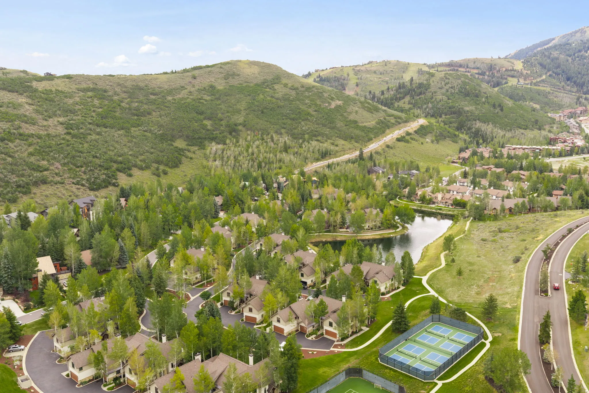 Community setting featuring a natural pond, residential structures with pitched roofs, tennis courts, and a paved road