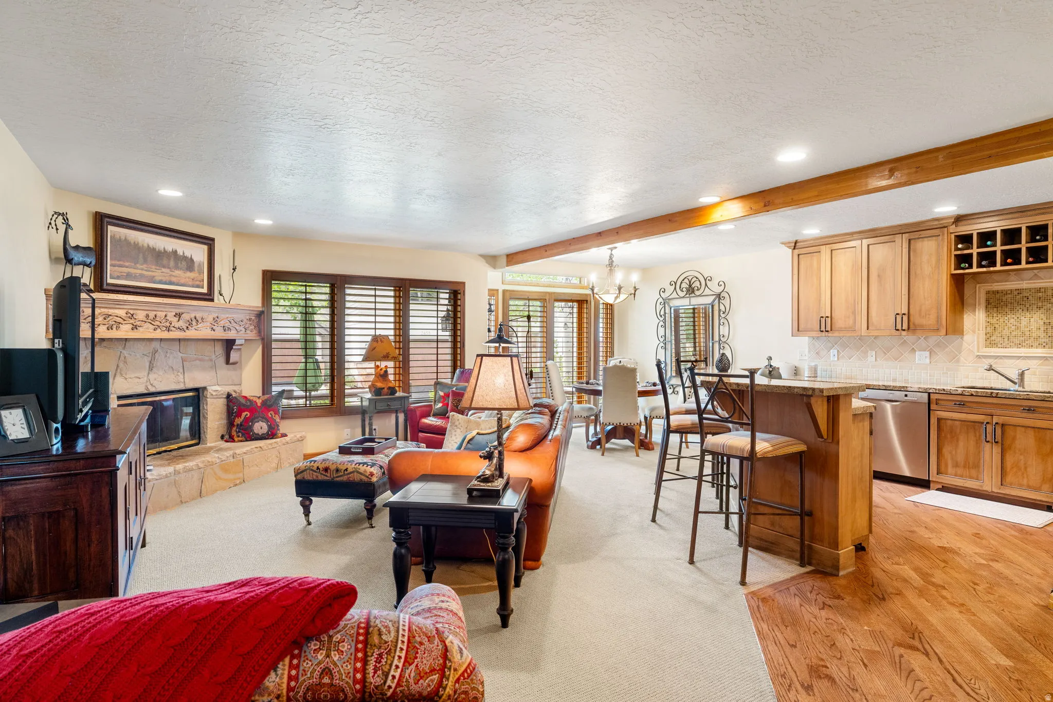 Stone-front fireplace, wood plank flooring, wood cabinetry with wine storage, recessed lighting, and a prominent wood beam