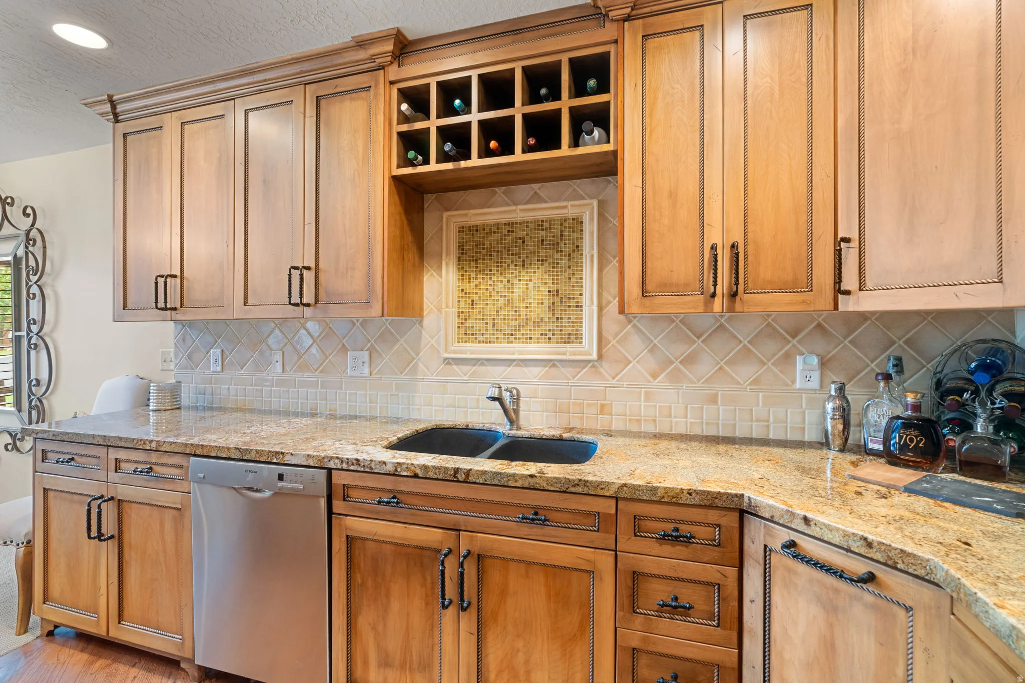 Expansive wood cabinetry with varied finishes, stone countertops, a built-in wine rack, tile backsplash, and a double basin sink