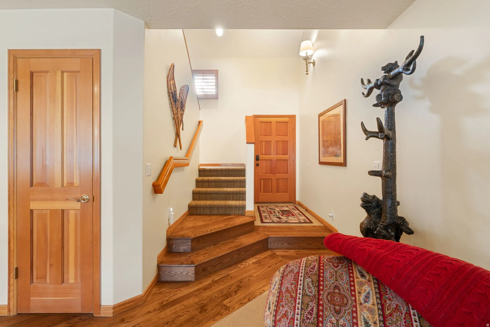 Wood-finish flooring, staircase with carpeted treads, wood paneled doors, and wall-mounted lighting