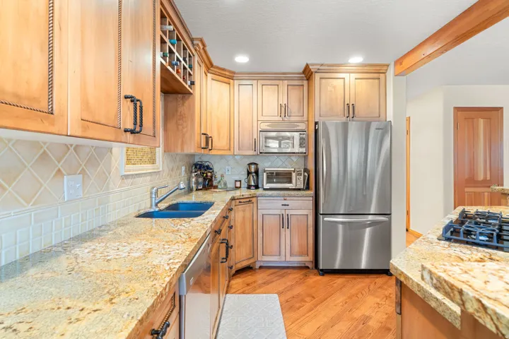 Kitchen featuring wood-finish cabinetry, granite countertops, tile backsplash, and stainless steel appliances