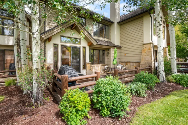 Stone and siding exterior with multiple patios, a stone chimney, a gabled window, and mature trees