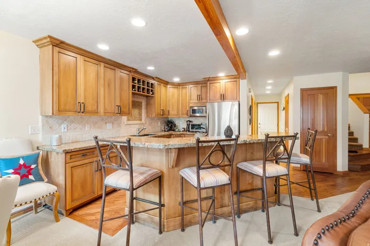 Kitchen featuring wood cabinetry, granite countertops, tile backsplash, built-in wine rack, and stainless steel appliances