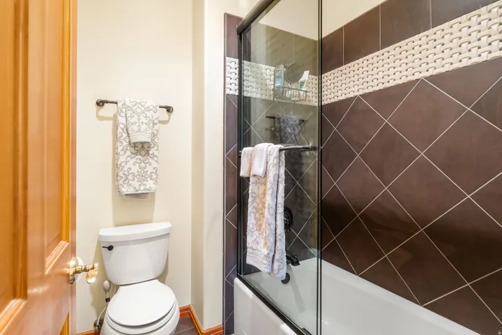 Shower-tub combination with glass enclosure, brown diamond-patterned wall tile, and decorative accent tile