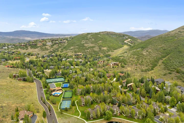 Expansive mountain landscape with scattered residential properties, mature trees, multiple tennis courts, and a swimming pool
