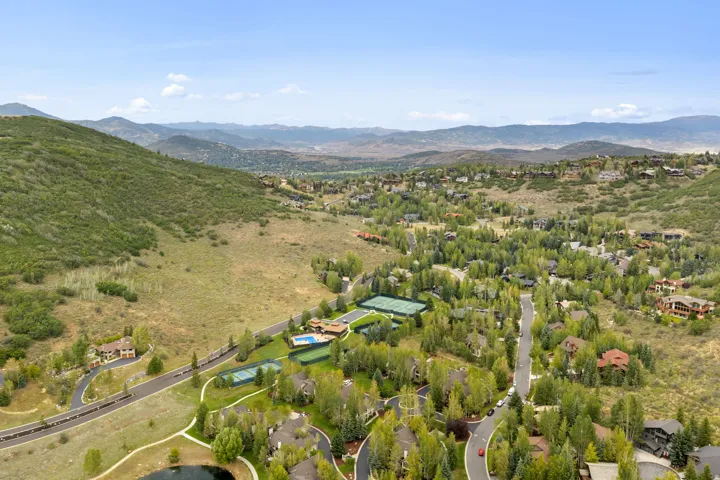 Expansive mountain landscape with scattered residential properties, mature trees, paved roadways, and a visible pond