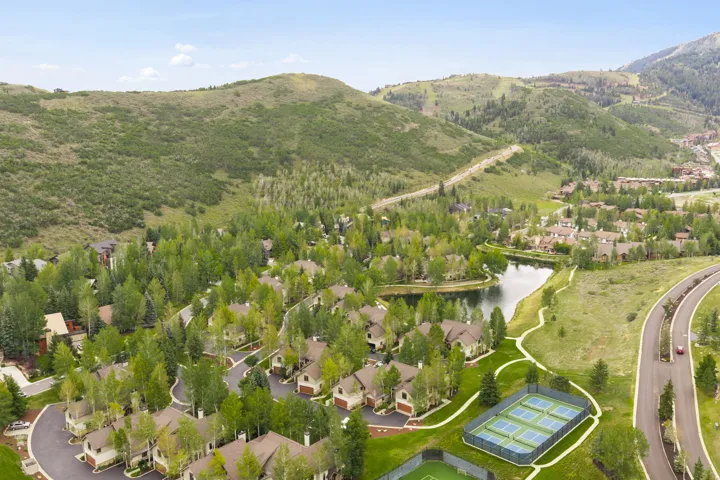 Community setting featuring a natural pond, residential structures with pitched roofs, tennis courts, and a paved road