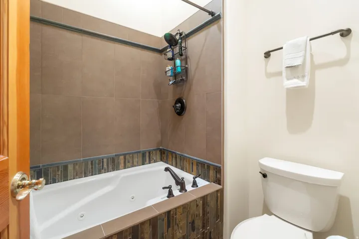 Soaking tub with bronze fixtures, natural stone tile surround, and large format wall tile