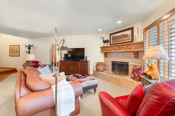 Stone-clad fireplace with an ornate wood mantel, natural light from a window with plantation shutters, recessed ceiling lighting, and light-toned wall finishes