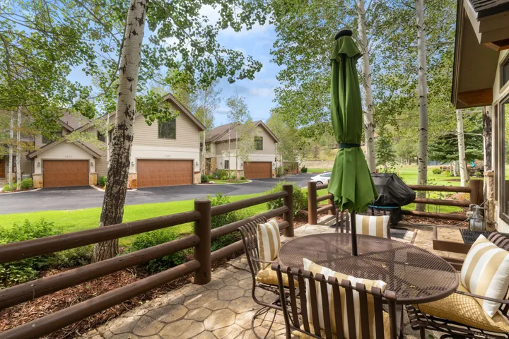 Stone-patterned patio featuring a log-style fence, mature trees, and a paved driveway leading to multi-car garages
