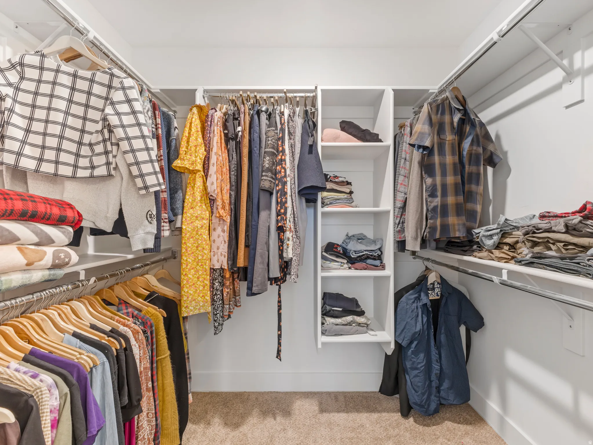 Walk-in closet featuring built-in shelving, multiple hanging rods, and neutral carpet flooring