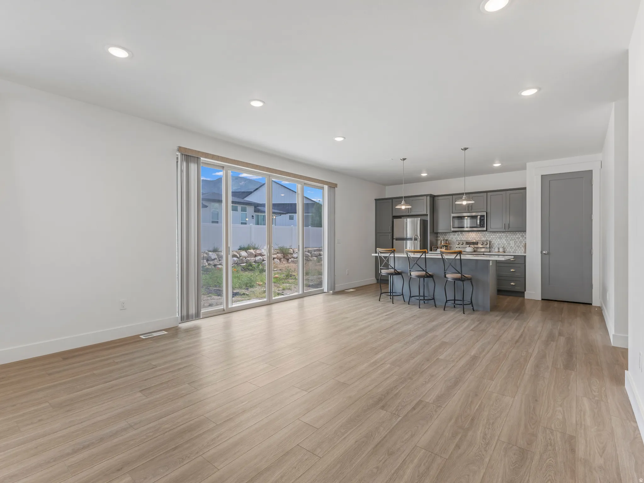 Open-concept living space featuring wood-finish flooring, recessed lighting, and a modern kitchen with gray cabinetry, stainless steel appliances, and a tiled backsplash