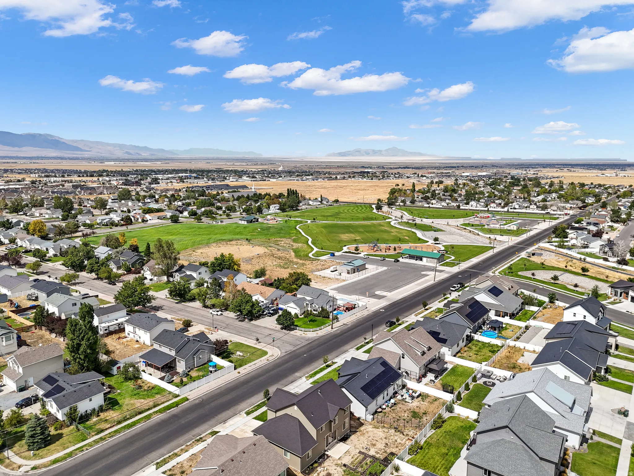 Aerial perspective showcasing a residential area with varied home styles, expansive green spaces, and mountain scenery in the distance