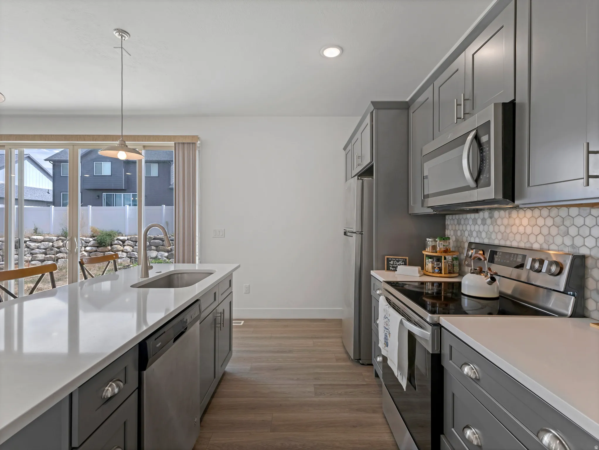 Modern kitchen featuring gray cabinetry, stainless steel appliances, a white hexagon tile backsplash, and a spacious island with a single-basin sink