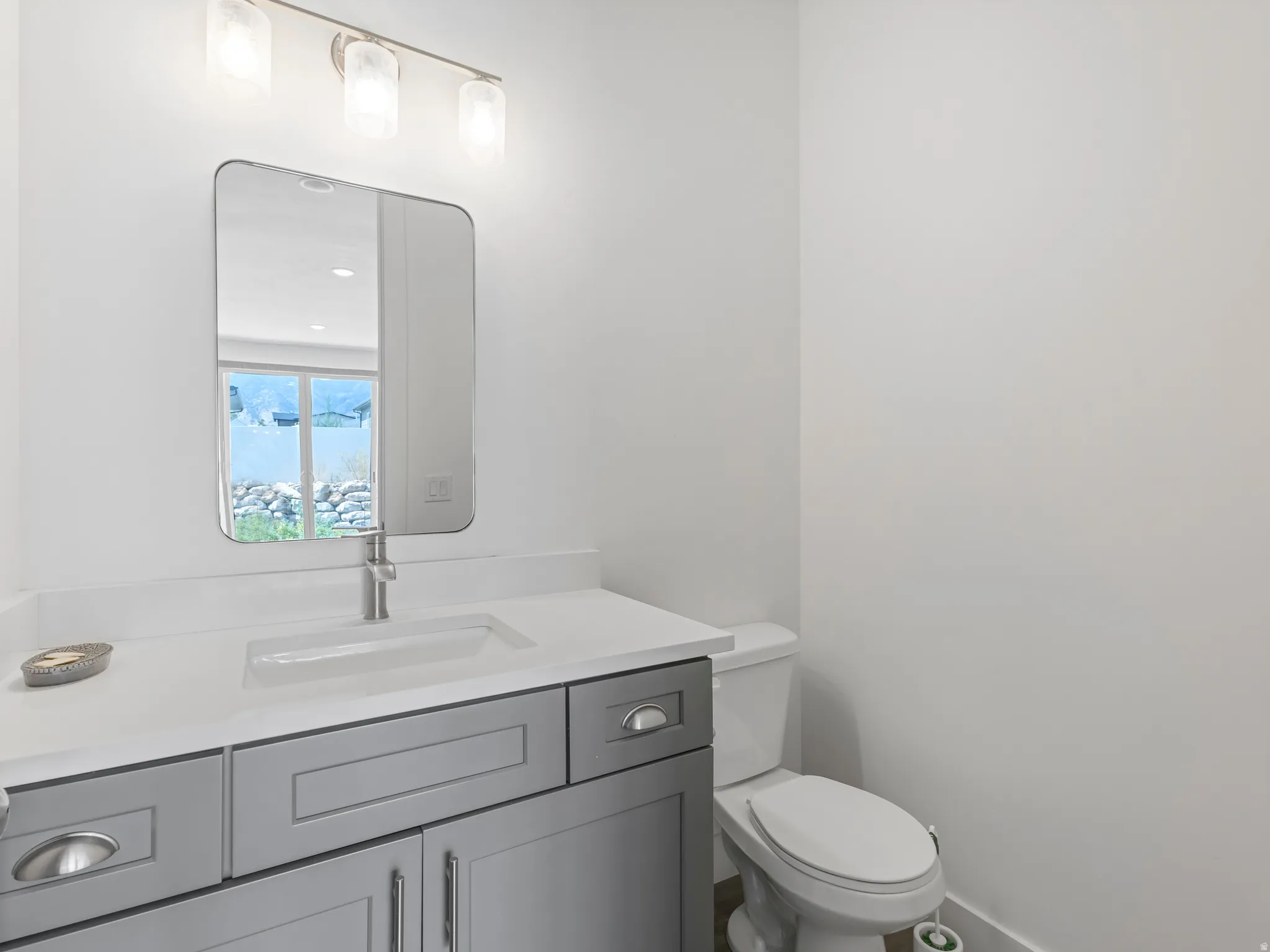 Vanity with gray shaker-style cabinetry, white countertop with integrated sink, brushed nickel faucet, and rectangular mirror