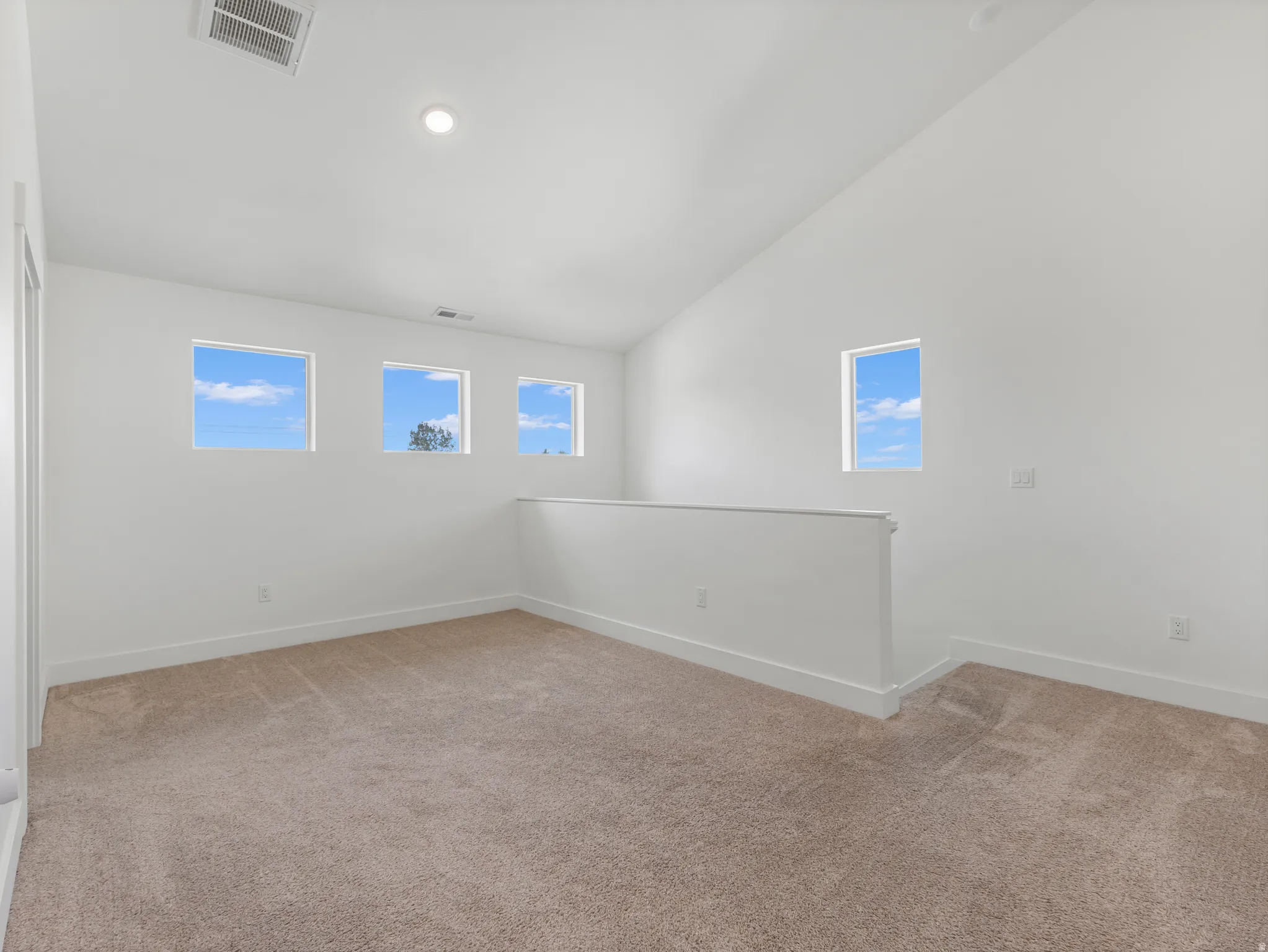 Vaulted ceiling, recessed lighting, neutral carpet, multiple windows, and a half-wall partition