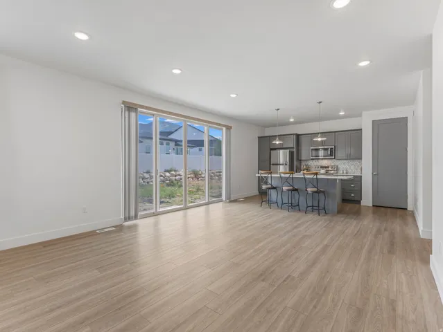 Open-concept living space featuring wood-finish flooring, recessed lighting, and a modern kitchen with gray cabinetry, stainless steel appliances, and a tiled backsplash