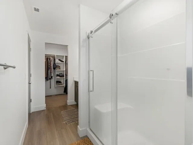 Sliding glass shower enclosure, wood-finish flooring, and a walk-in closet with built-in shelving