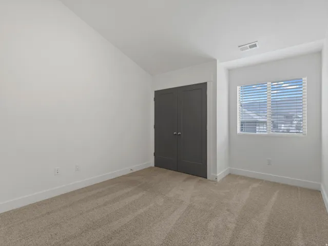Vaulted ceiling, neutral tone carpet, window with blinds, bi-fold closet doors, white walls