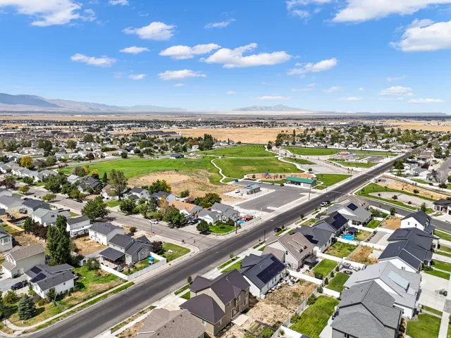 Aerial perspective showcasing a residential area with varied home styles, expansive green spaces, and mountain scenery in the distance