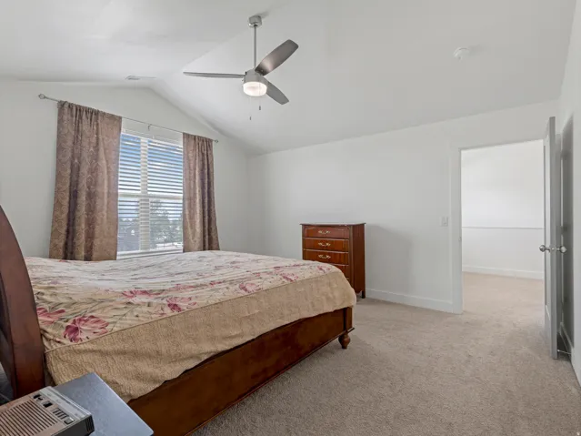 Vaulted ceilings with a ceiling fan, carpet flooring, a large window, and white walls