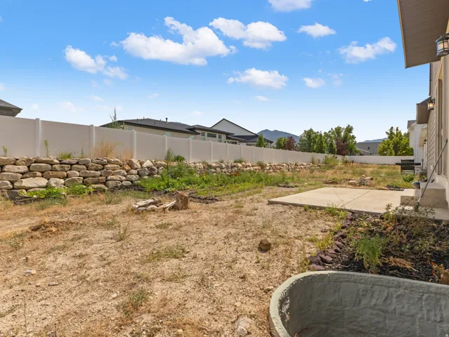 Rear exterior featuring a concrete patio, retaining wall, and perimeter fencing
