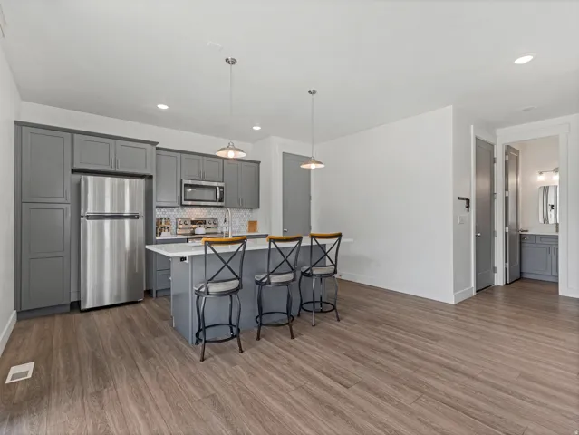 Kitchen featuring wood-finish flooring, gray cabinetry, stainless steel appliances, and a central island with pendant lighting