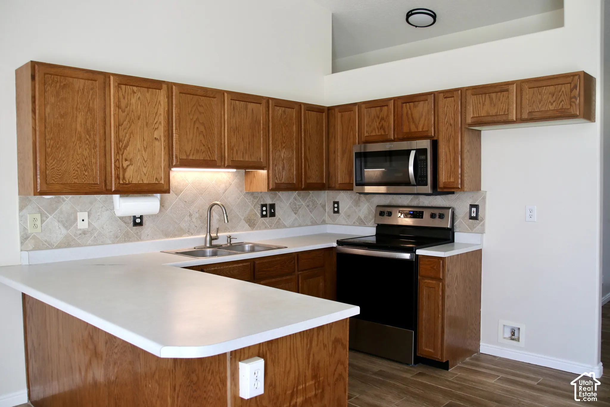 U-shaped kitchen with wood-finish cabinetry, solid surface countertops, and backsplash