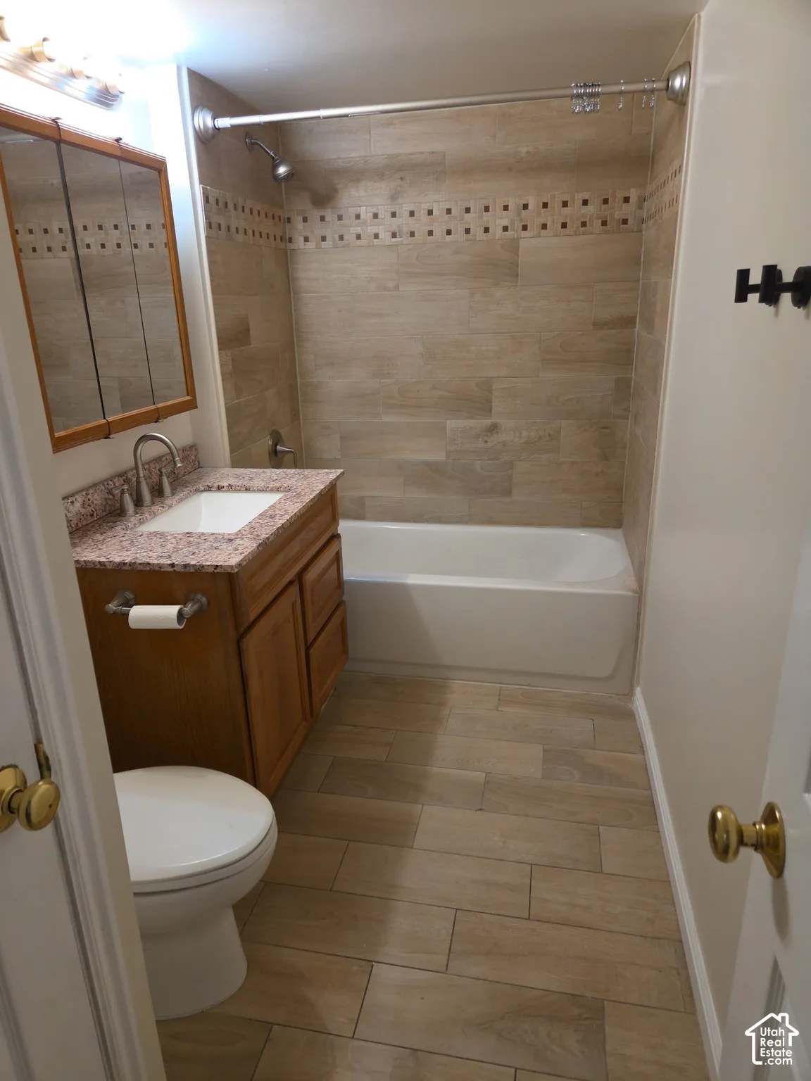 Bathroom featuring wood-finish tile flooring, a built-in vanity with a granite-style countertop, a framed medicine cabinet, and a tiled shower surround with accent detailing