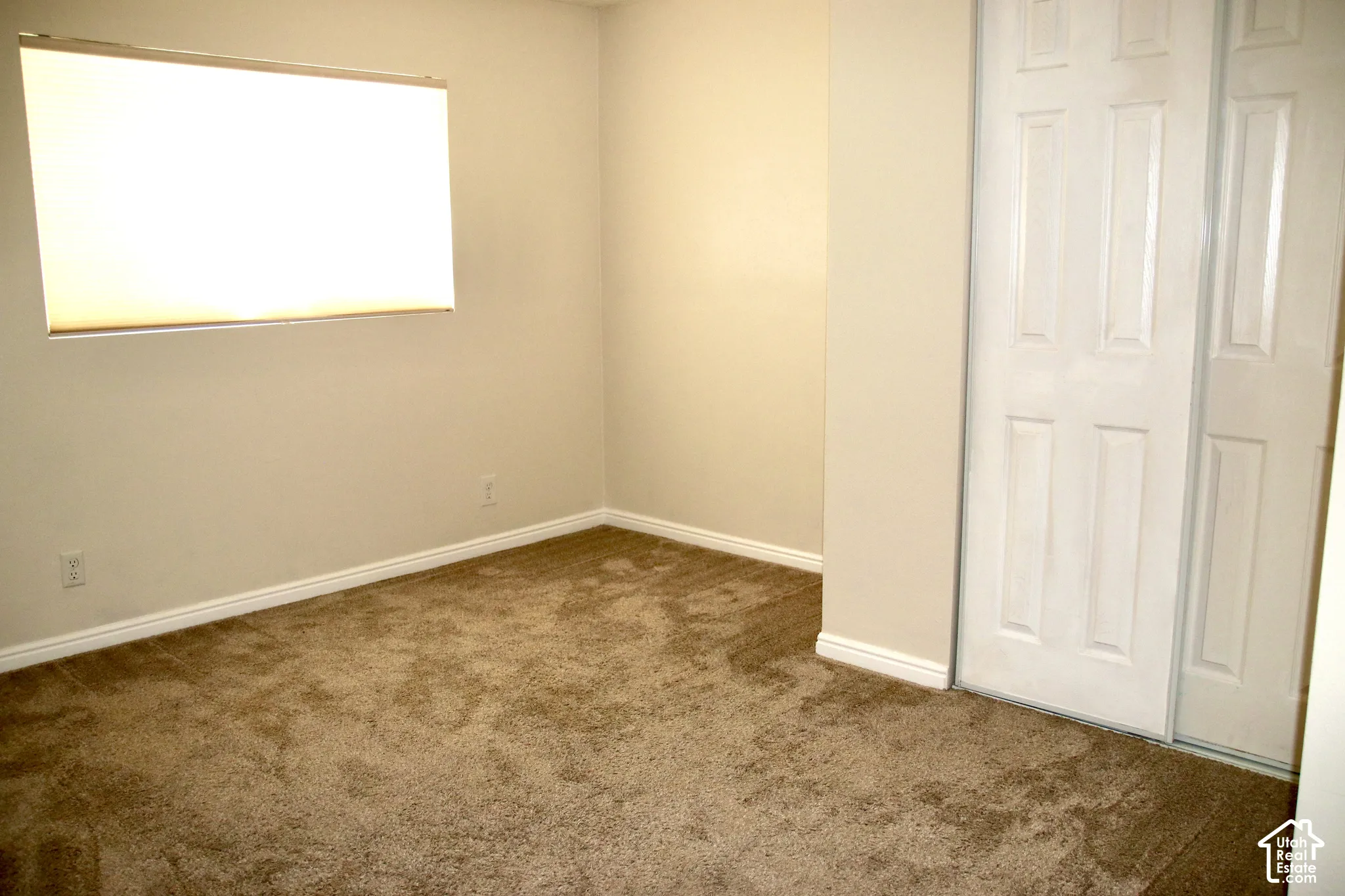 Carpeted flooring, neutral wall tones, window with roller shade, and bi-fold closet doors