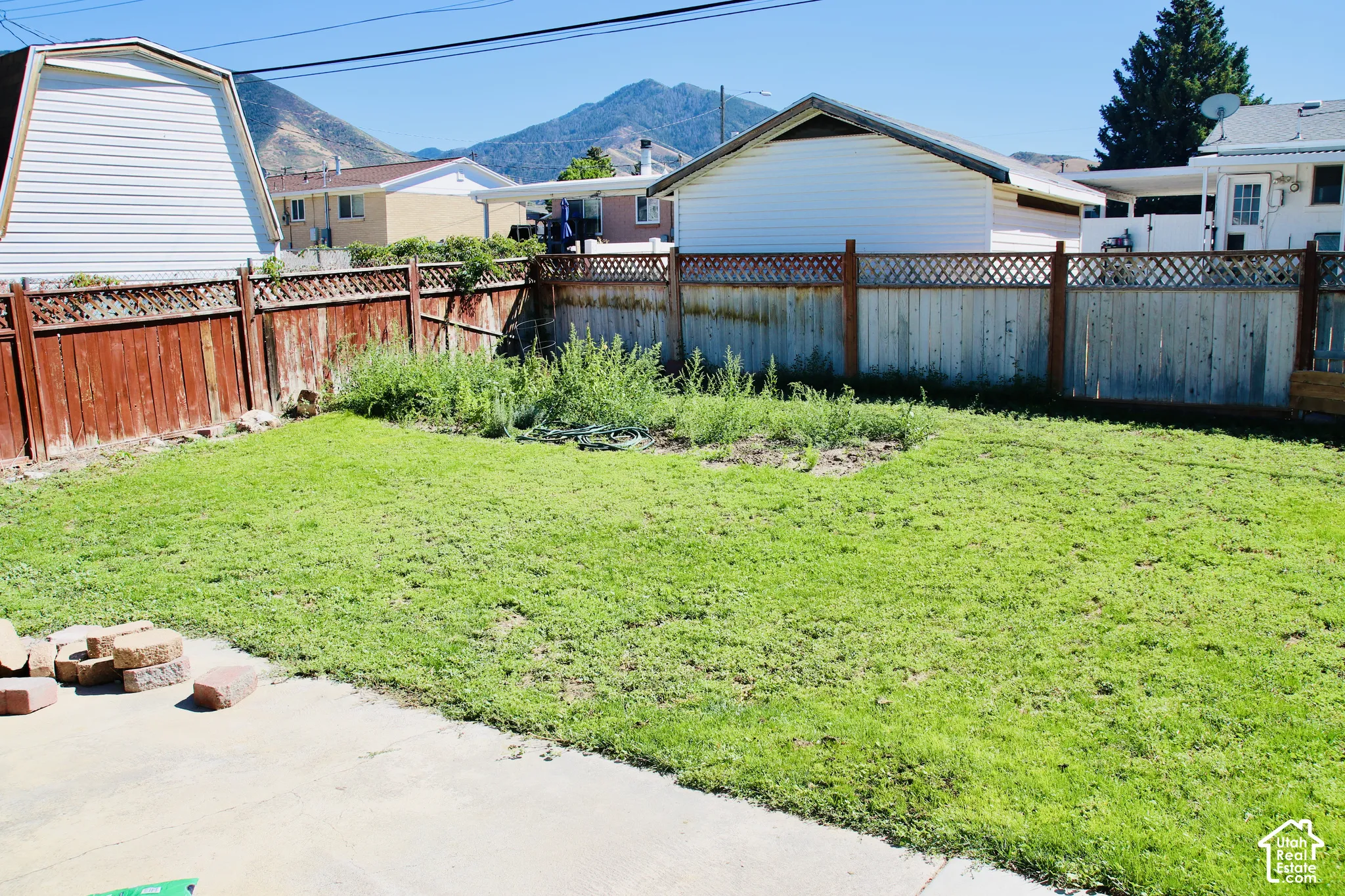 Expansive grassy area with a large concrete patio and wood fencing