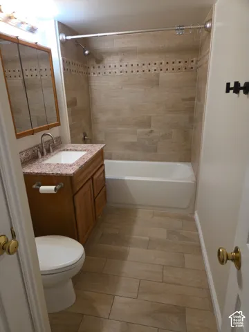 Bathroom featuring wood-finish tile flooring, a built-in vanity with a granite-style countertop, a framed medicine cabinet, and a tiled shower surround with accent detailing