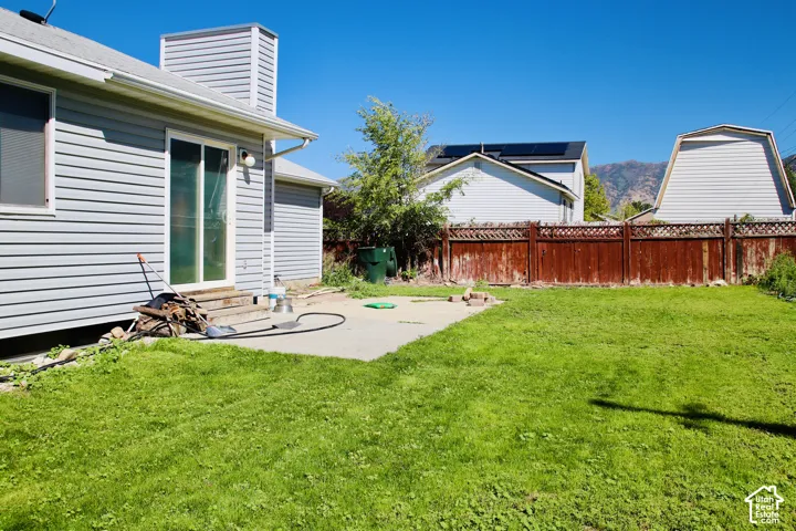 Expansive rear yard with a concrete patio, wood privacy fence, and mature landscaping