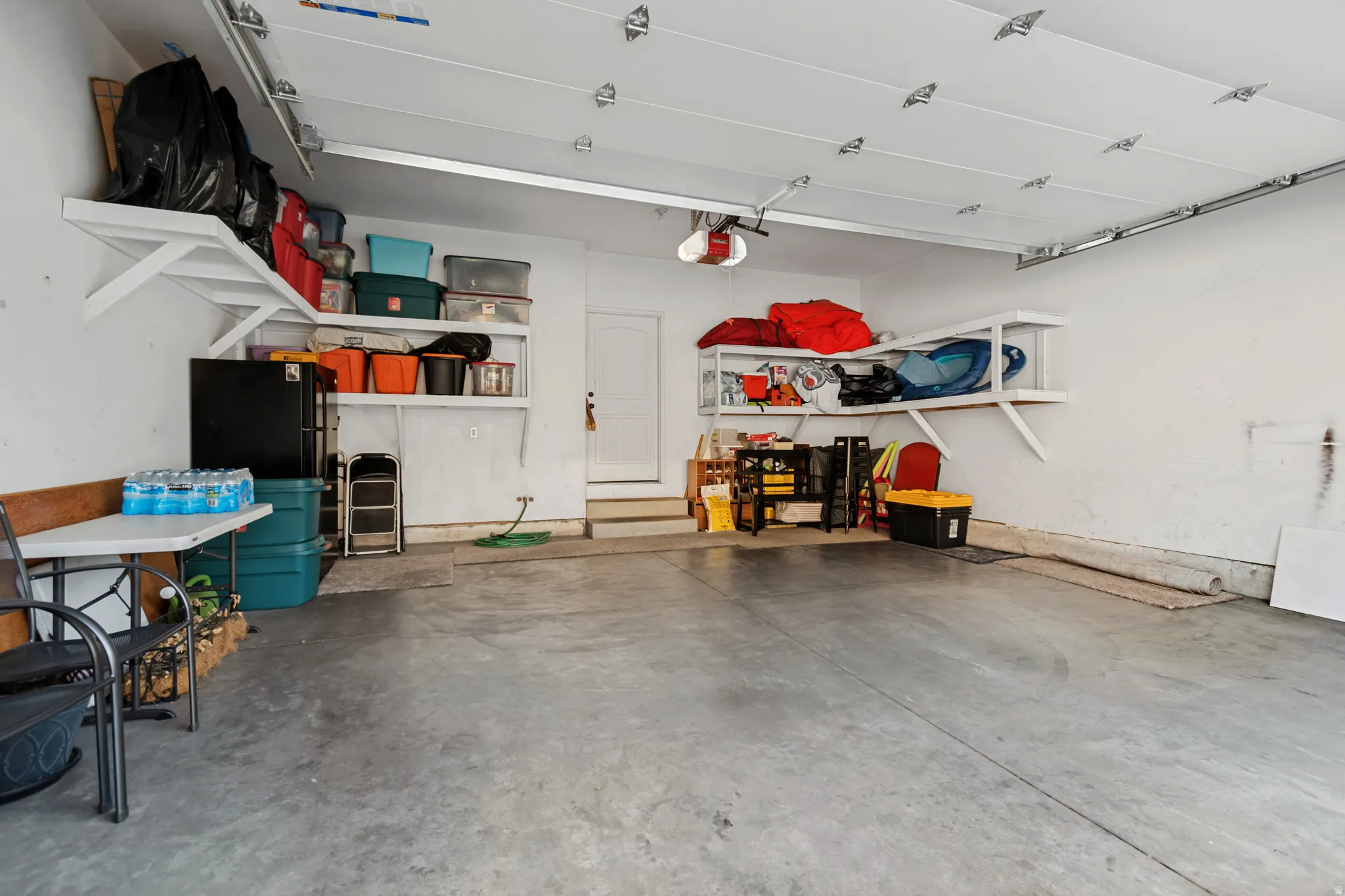 Concrete flooring, white walls, built-in shelving, and garage door opener