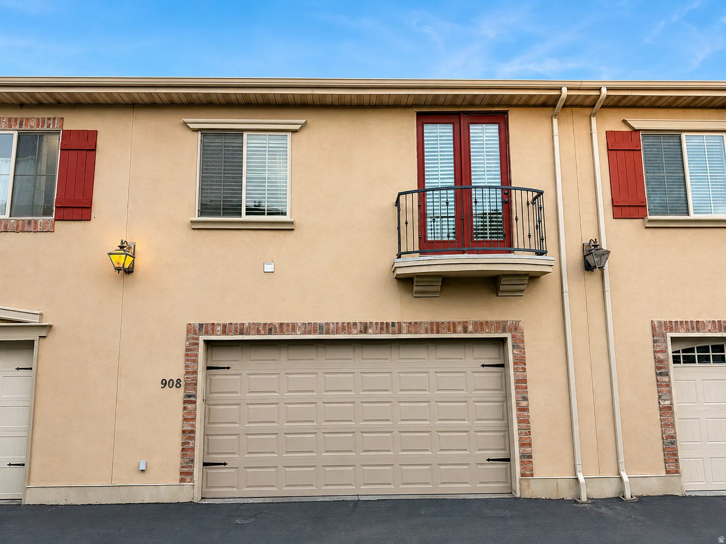 Stucco exterior with brick detailing, a garage door, and a second-level balcony with French doors