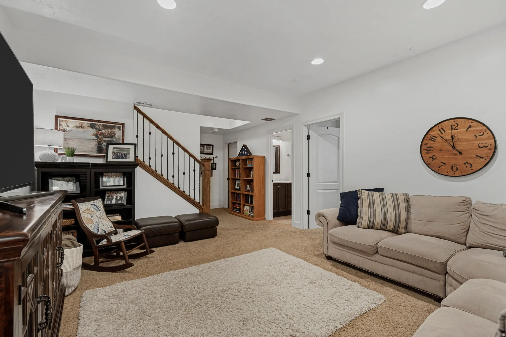 Carpeted living space with recessed lighting, featuring a wood and wrought iron staircase