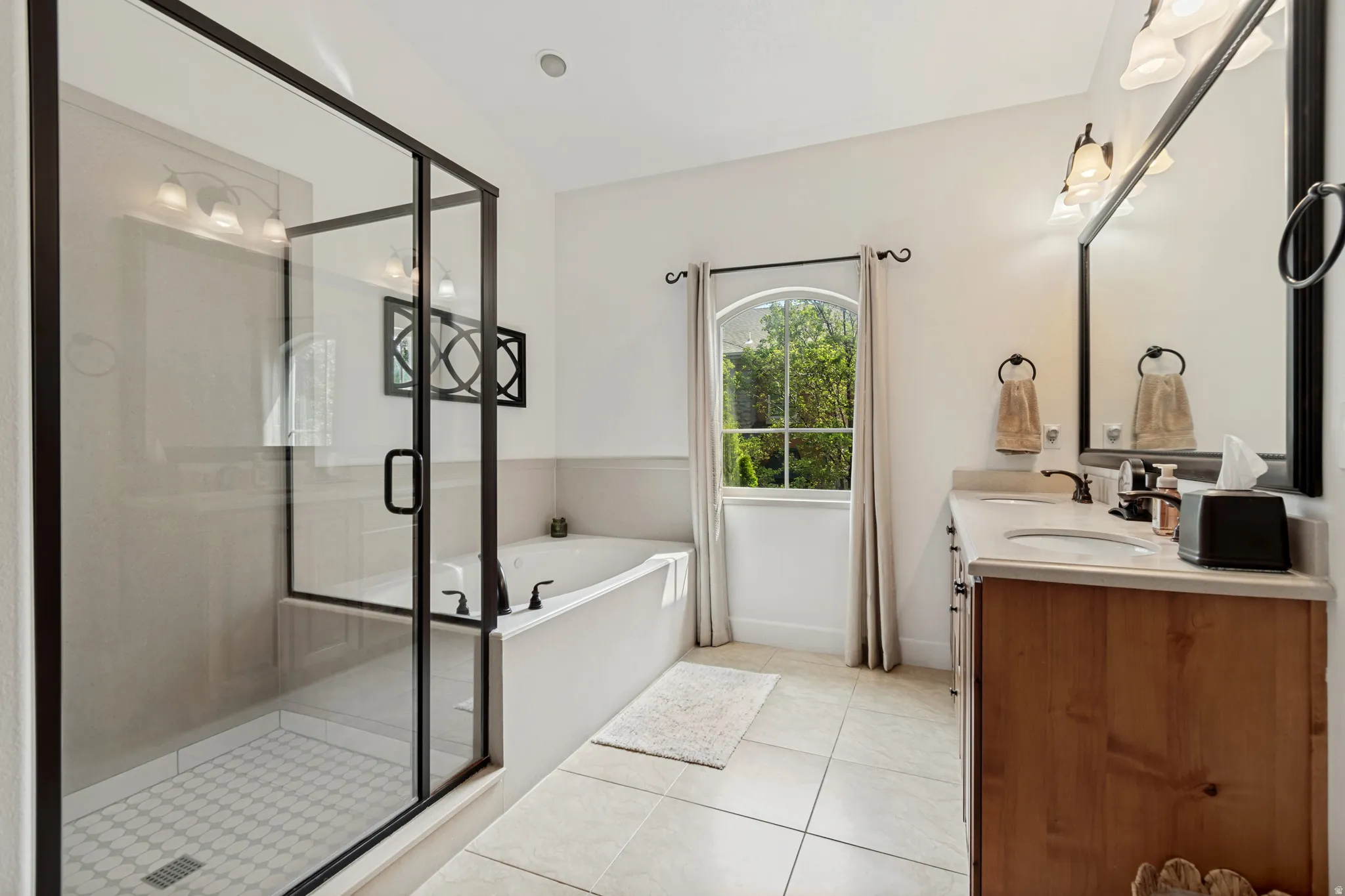 Glass-enclosed shower with mosaic tile flooring, a soaking tub, a single vanity with a solid surface countertop, and a tall arched window