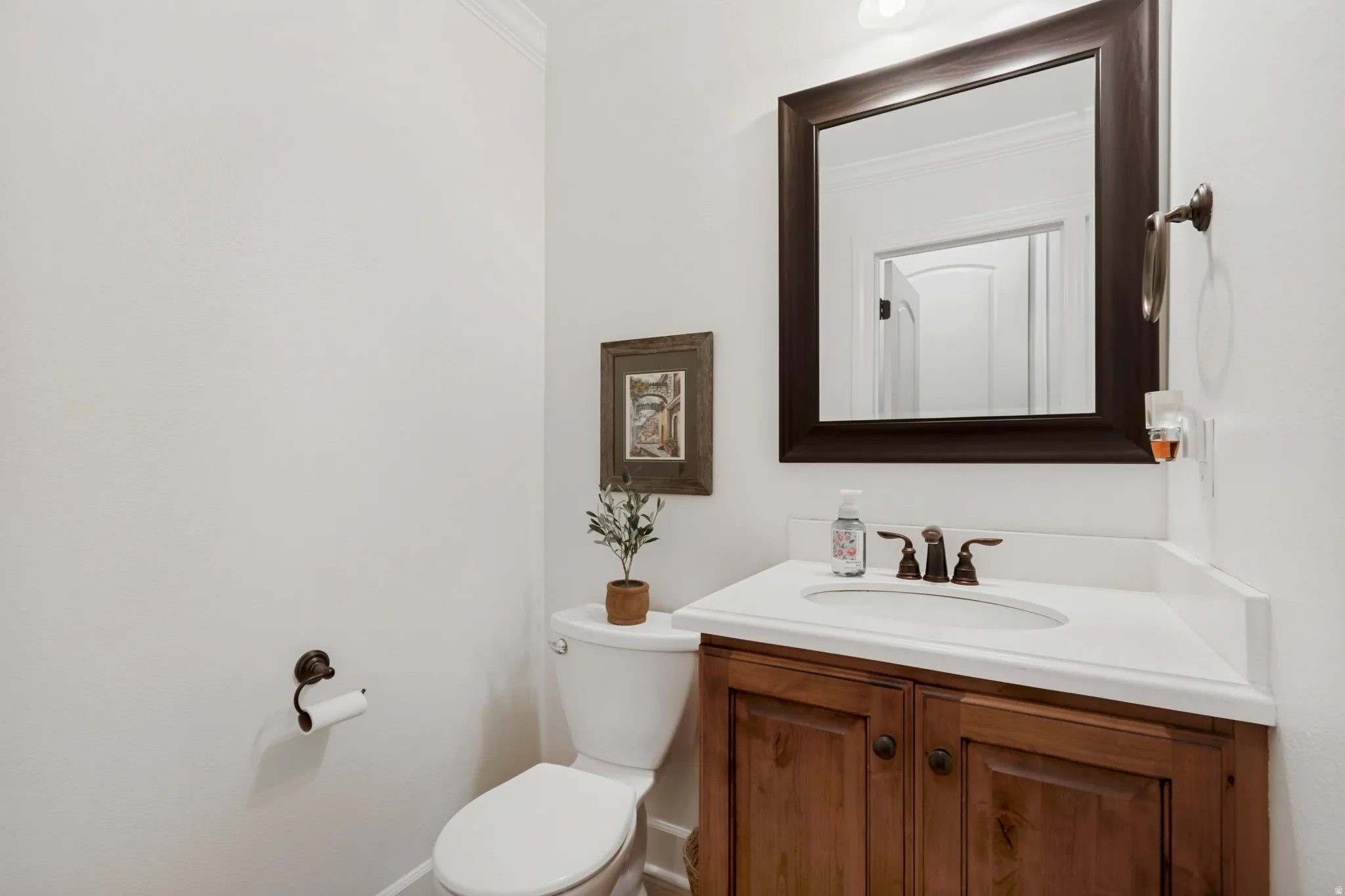 Wood-finish vanity with white countertop and oval sink, bronze-finish faucet, and coordinating framed mirror