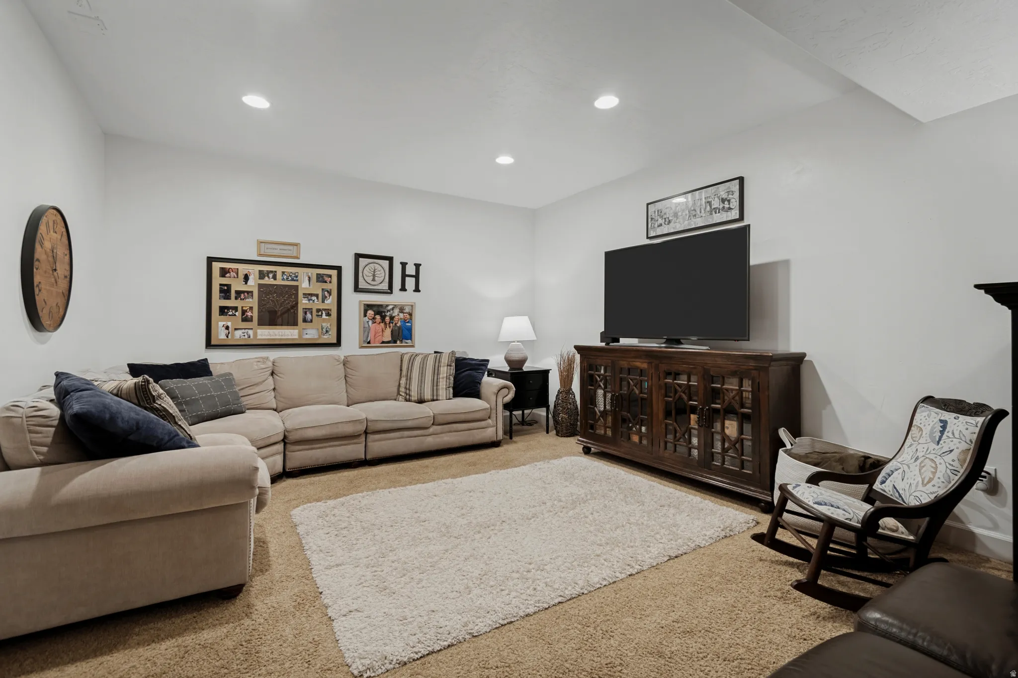 Recessed lighting illuminates this carpeted room, featuring white walls and a dark wood media console