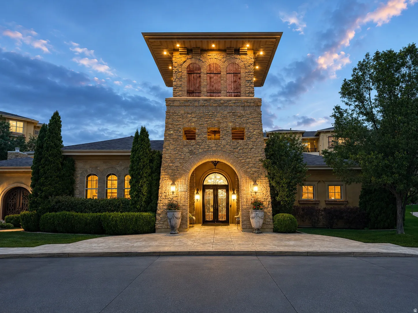 Clubhouse stone facade with arched entry, wrought iron double doors, and an illuminated tower with decorative shutters