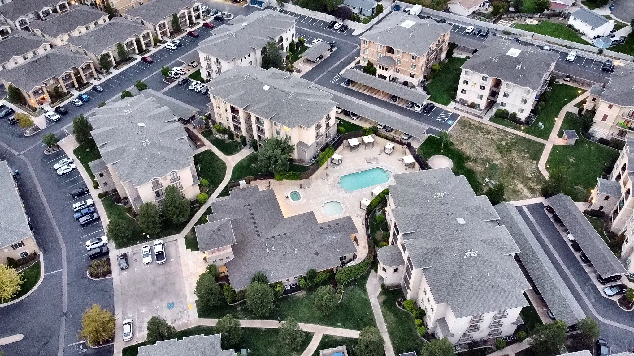 Clubhouse aerial views. Community featuring multiple buildings, surface parking areas, covered parking structures, a swimming pool, and a spa