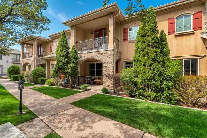 Stucco exterior with stone accents, arched entryways, private balconies with wrought iron railings, and red window shutters