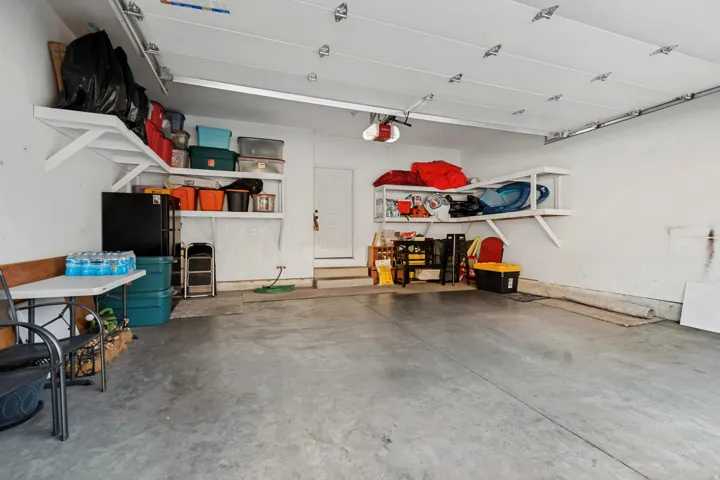 Concrete flooring, white walls, built-in shelving, and garage door opener